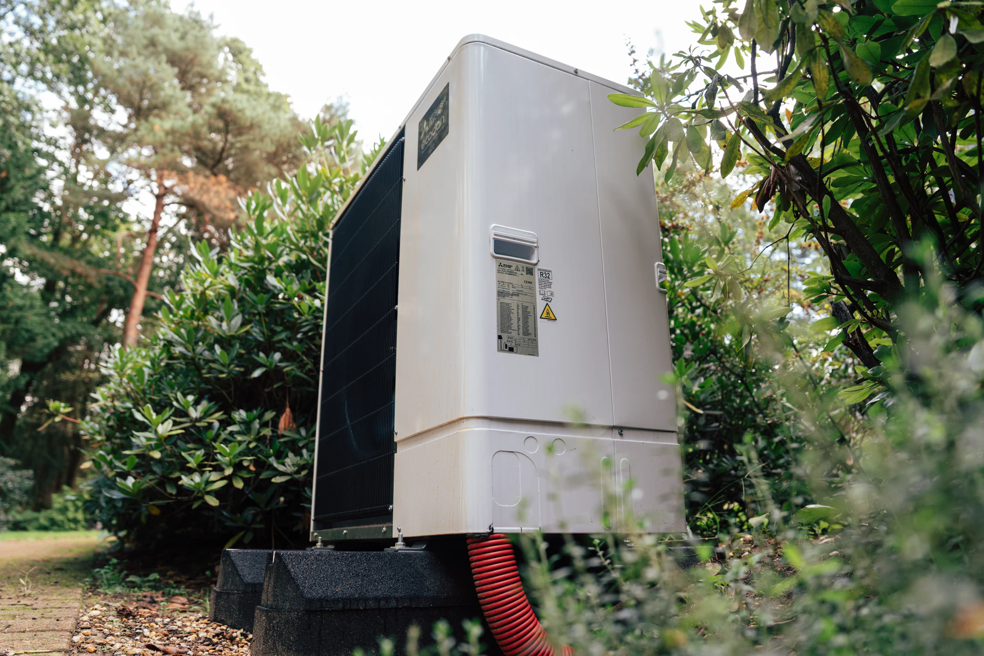 Buitenunit van een warmtepomp tussen het groen